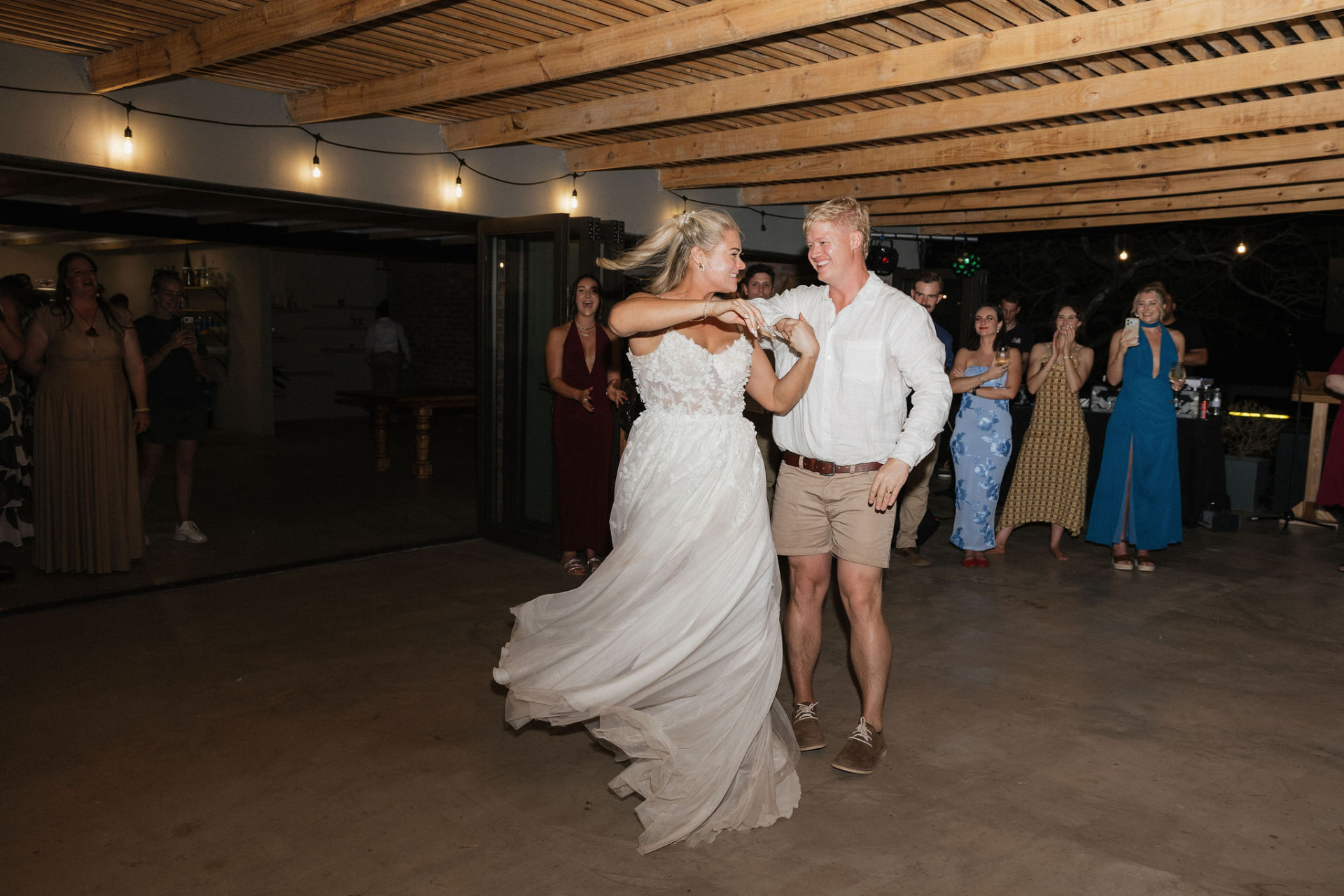 The newlyweds' first dance on the lit patio as guests look on