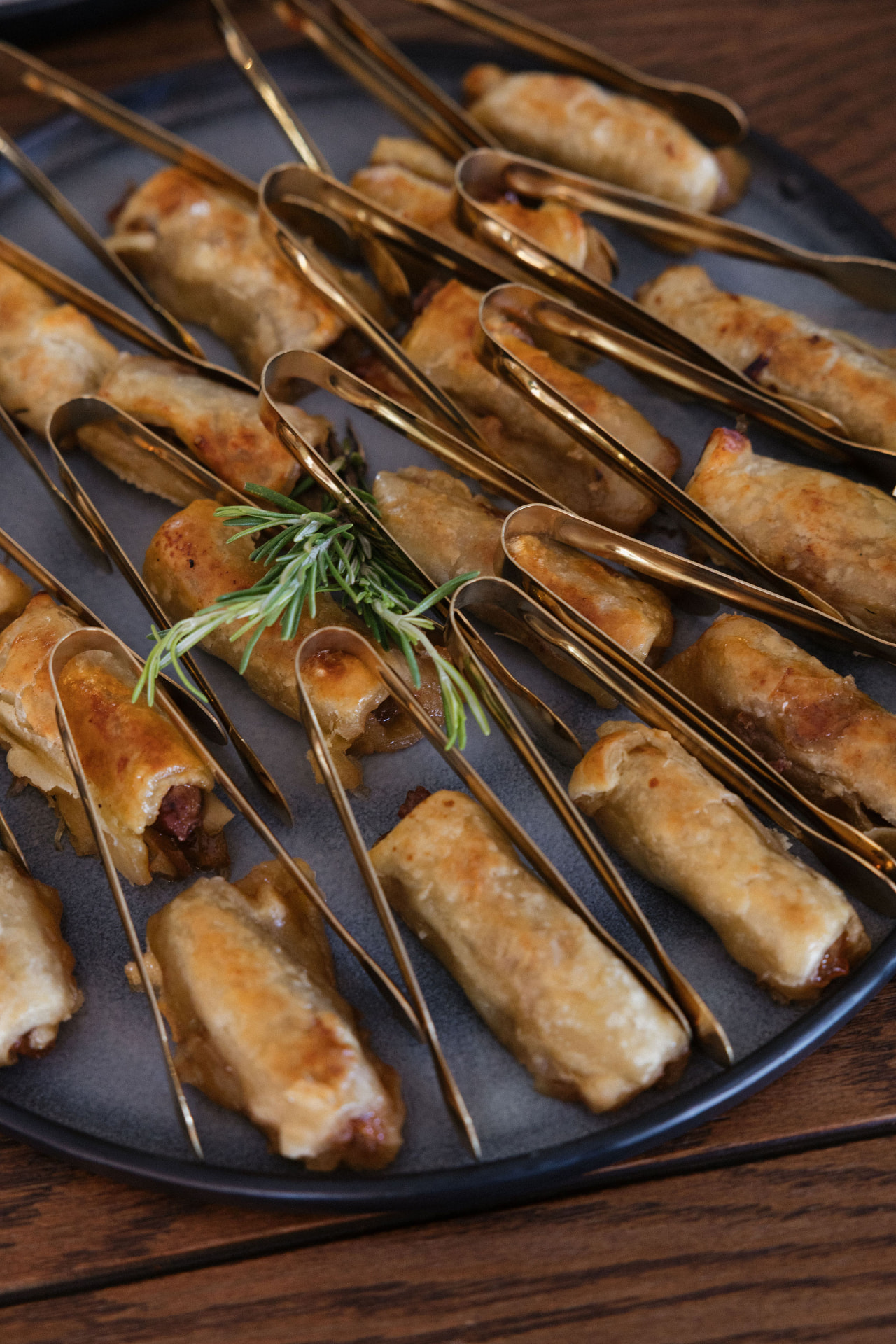 Golden tongs serving warm canapés on a slate platter