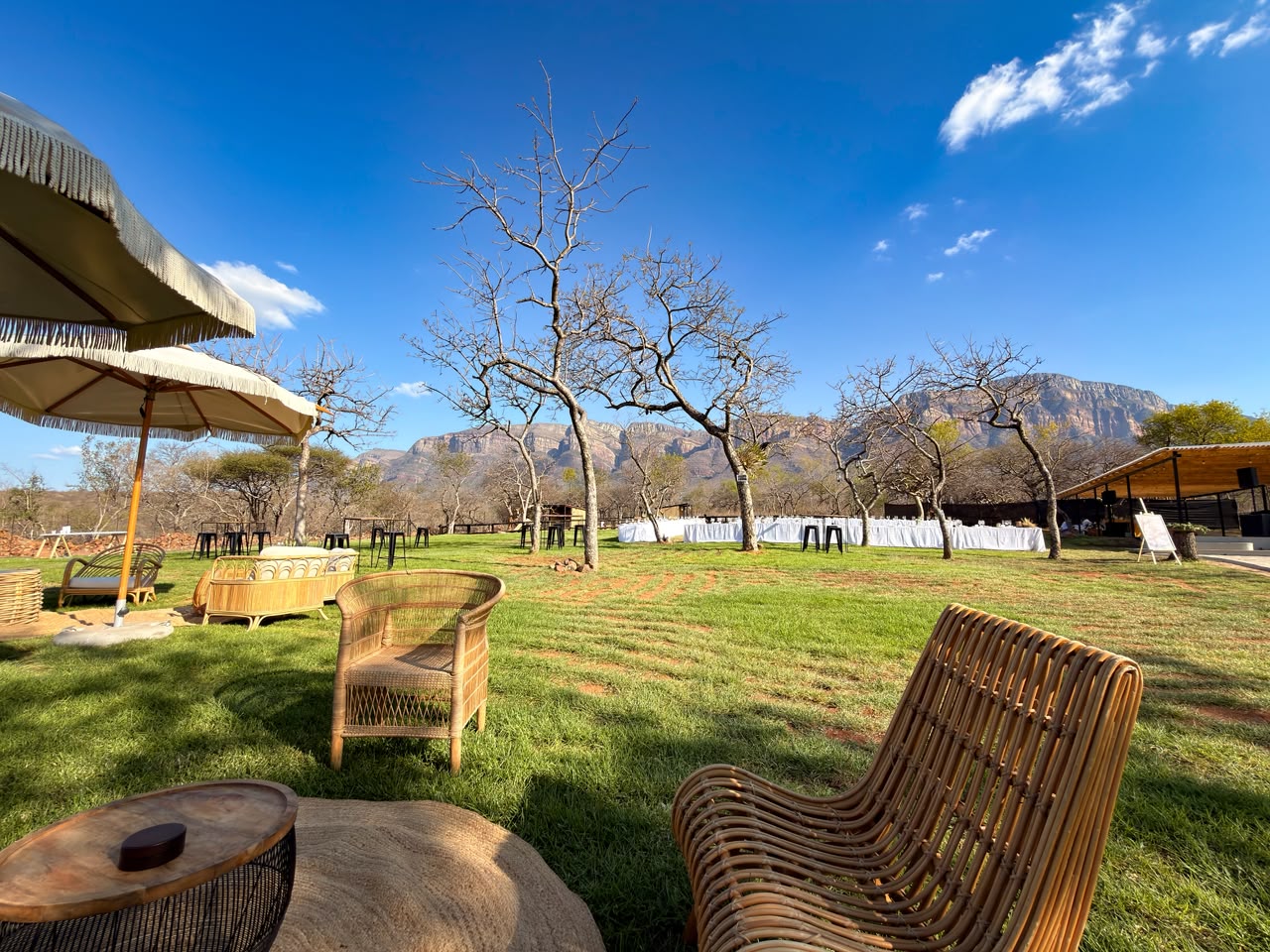 Long banquet tables and wicker lounge seating set on the cafe lawn beneath the mountains at MyAfrica Farm