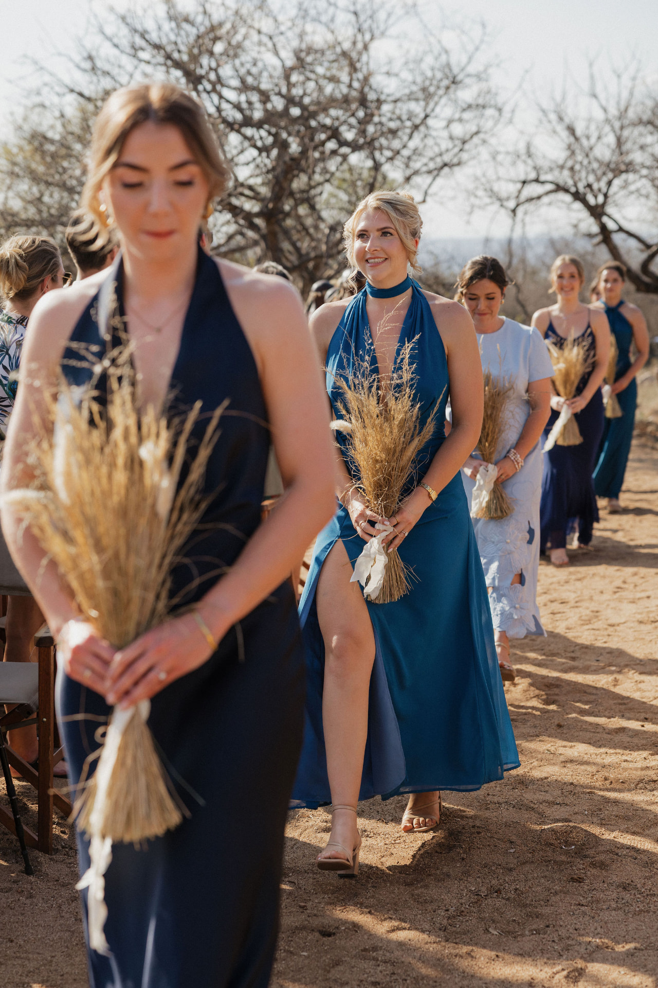 Bridesmaids in blue walking the aisle with dried-grass bouquets